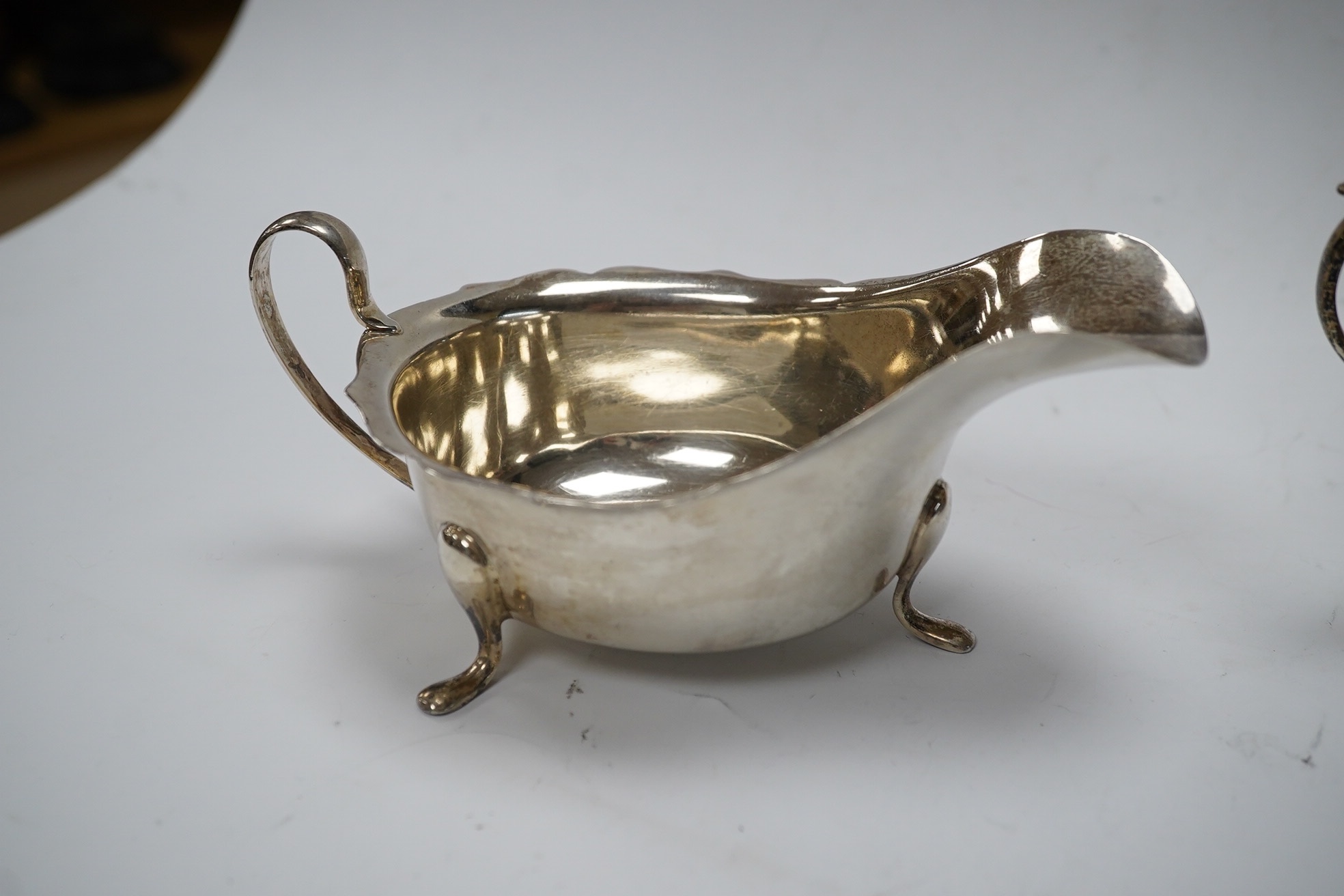 A George III Scottish silver cream jug, later embossed, a pair of George V silver sauce boats and an Edwardian hammered silver two handled porringer, by Moss Morris,18.4oz. Condition - poor to fair